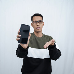 A young Asian man with glasses wearing a sweater points to a smartphone screen. Isolated on a white background.