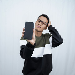 A young Asian man with glasses wearing a sweater points to a smartphone screen. Isolated on a white background.