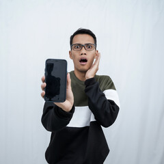 A young Asian man with glasses wearing a sweater points to a smartphone screen. Isolated on a white background.