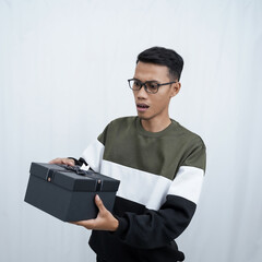 An Asian young man with glasses wearing a sweater with a surprised happy expression getting a surprise gift. Isolated on a white background.