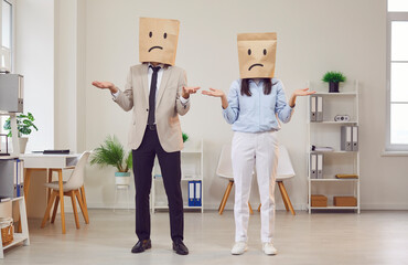 Portrait of two confused business people coworkers standing indoors with paper bags on head with...