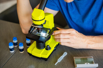 Close up view of hands of man examining various samples under a microscope at home as a hobby....