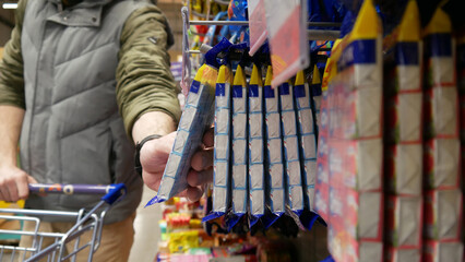 A male consumer with a shopping cart taking a pack of candies from the retail display