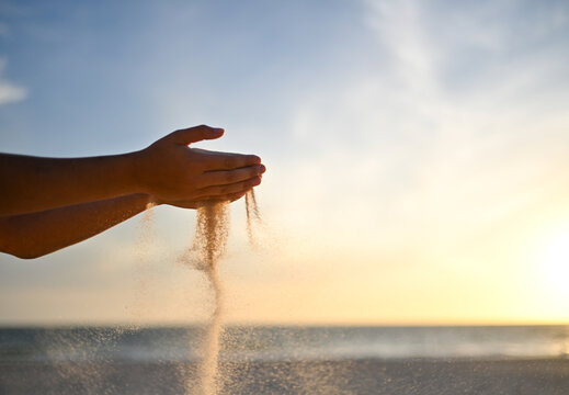 Sand falling through boy's hands with ocean sunset in the background