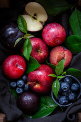 Aerial view of red apples, plums, and blueberries with green leaves