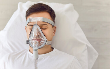 Young adult man lying on a hospital couch, sleeping and breathing through an oxygen mask. Medical...