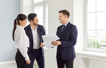 Professional cheerful real estate male agent showing new apartment to young couple. Man and woman...