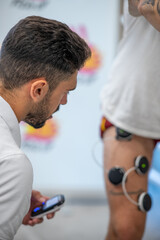 Fototapeta premium Osteopath practising physiotherapy at the gym on a man's leg with the help of electrodes