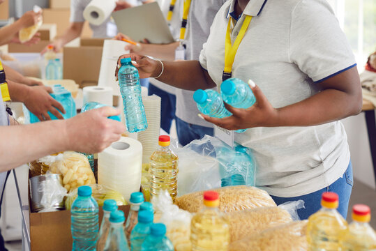 Diverse volunteers group sorting donations of foodstuffs in cardboard boxes for charity food drive. People volunteering in food bank working in charitable foundation together. Humanitarian aid