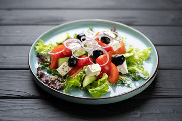 Mediterranean salad with cheese vegetables and olives on plate on wooden background