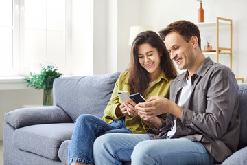Smiling family couple using mobile phones, sharing each other phone content. Happy husband and wife...