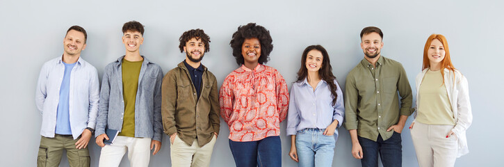 Banner with a group portrait of happy diverse people posing by a gray wall. Team of smiling Caucasian and African American men and women in casual clothes standing on a gray color background