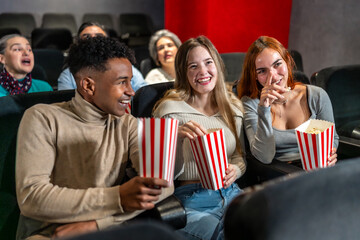 Friends enjoying watching movie and eating popcorn in cinema