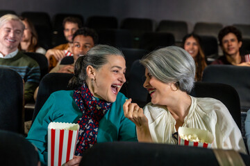 Two smiling senior women enjoying a movie at the cinema with popcorn