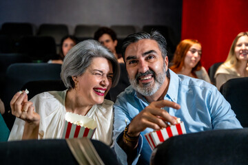 Senior couple laughing and eating popcorn, enjoying a movie at the cinema