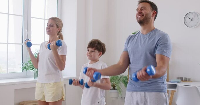 Sporty happy family doing morning training, beautiful sporty healthy people, enjoy fitness exercises with dumbbells, workout at home, doing weight training, group of friendly parent and small kid 