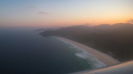 A stunning aerial view of a beach during sunset with waves and mountains in the background.