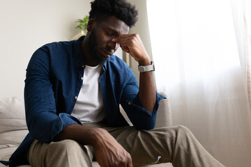 Tired Black man sitting on the sofa, having headache. Copy space.