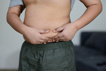 A fat child with a fat belly holds his stomach with his hands.