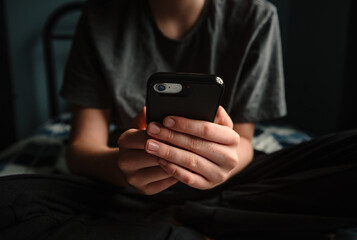 Close up of hands of teen boy holding smartphone sitting on bed.