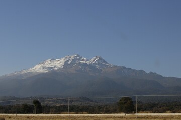 paisaje de monta&ntilde;a con nieve y arboles, con postes de luz en la carretera y fondo de cielo azul