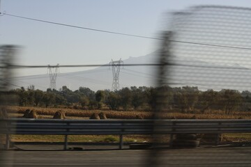 campo de cultivo con torres eléctricas arboles y muro de contención de la carretera con cercado o...