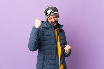 Skier man with snowboarding glasses over isolated purple background celebrating a victory