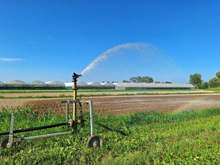 A moving sprinkler on wheels irrigates rural fields. Rainbow when watering beds.