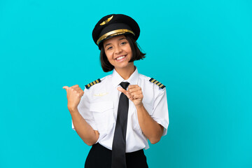 Young airplane pilot over isolated blue background pointing to the side to present a product