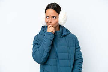 Young hispanic woman wearing a winter earmuffs isolated on white background having doubts and with...