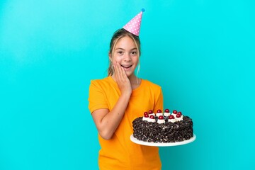 Little caucasian girl holding birthday cake isolated on blue background with surprise and shocked...