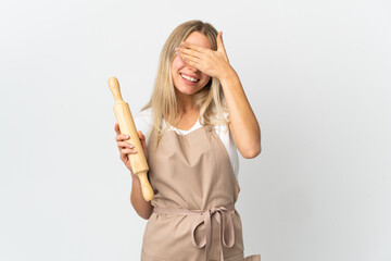 Young woman holding a rolling pin isolated on white background covering eyes by hands