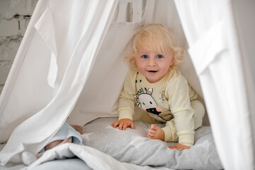 Little blond boy playing with toys at home. Children's game concept. Cheerful naughty boy sitting...