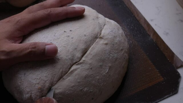 Baker hand scoring dough with a razor blade before bake sourdough bread. 
