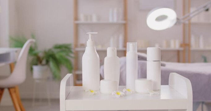 White bottles, cream jars and cosmetic skin care products for female skin and body care in empty beauty spa salon room. Spa treatment, wellness and cosmetology concept. 4k video. Slow motion video.