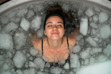 Woman practices cold therapy in an outdoor ice bath surrounded by tropical plants. A peaceful moment of self-care and healing