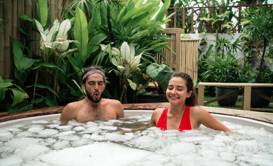 Man and woman take an ice bath outdoors in a tropical setting. Cold plunge for health, recovery,...