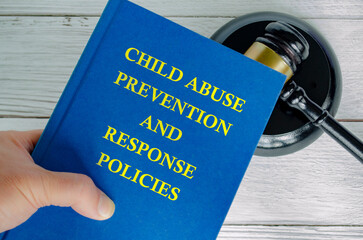 Hand holding Child Abuse Prevention and Response Policies book with gavel background