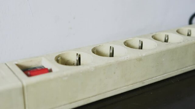 Male hand unplugging the plug from socket electric extension cord and turn off the power switch.