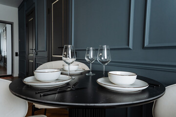 A beautifully arranged dining room table that features elegant plates, decorative bowls, and stylish wine glasses placed neatly across its surface, creating a welcoming atmosphere for meals