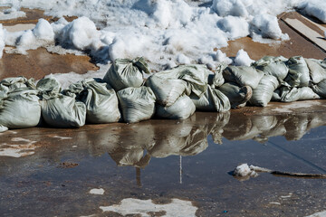A sizable puddle surrounds several sandbags, which are susceptible to changes in temperature and...