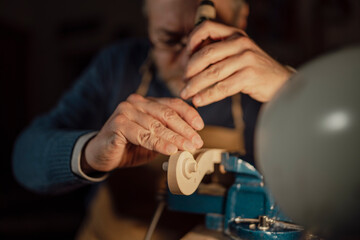 Skilled luthier carefully carving violin scroll with traditional hand tools, revealing intricate woodworking expertise in classic workshop setting
