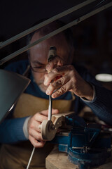 Skilled luthier carefully carving intricate violin scroll using specialized gouge, wooden workspace...
