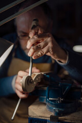 Skilled luthier carving intricate violin scroll, hands carefully guiding sharp gouge under workshop lamp, revealing meticulous craftsmanship of stringed instrument creation