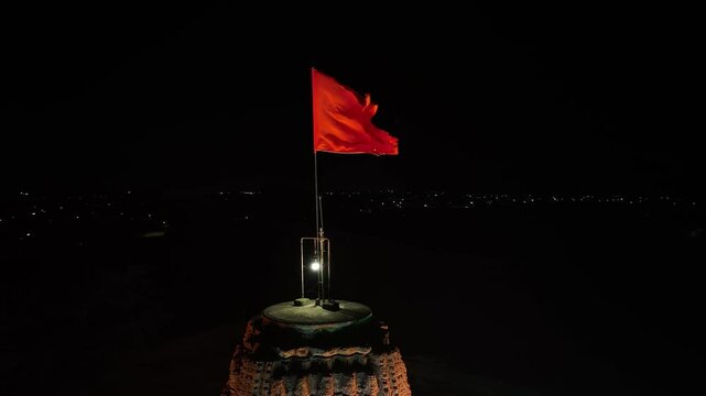 illuminated orange flag on ancient Hindu temple. waving prominently against a calm night sky. The aerial drone video captures a profound sense of historical importance and cultural pride.