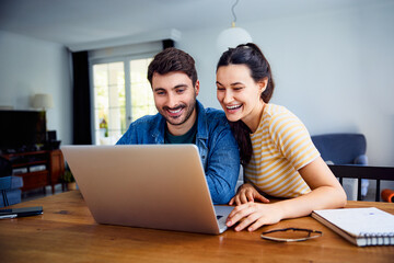 Excited young couple using laptop together at home sitting at a table