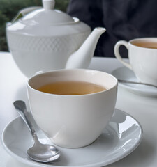 tea time elegance, a white teacup filled with tea sits on a saucer with a spoon, next to a teapot and another cup, creating an elegant setting