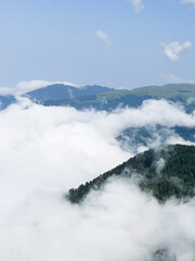 mountain peak view, the forested mountain rises above dense clouds, revealing distant hills and a...