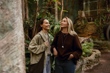 A young White woman in her late 20s, with long blond hair, standing in a forest section of a...