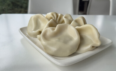 elegant dumpling presentation, steamed dumplings are neatly arranged on a white plate, with smooth, doughy exteriors suggesting they may be filled with meat or vegetables a white table, chairs, and